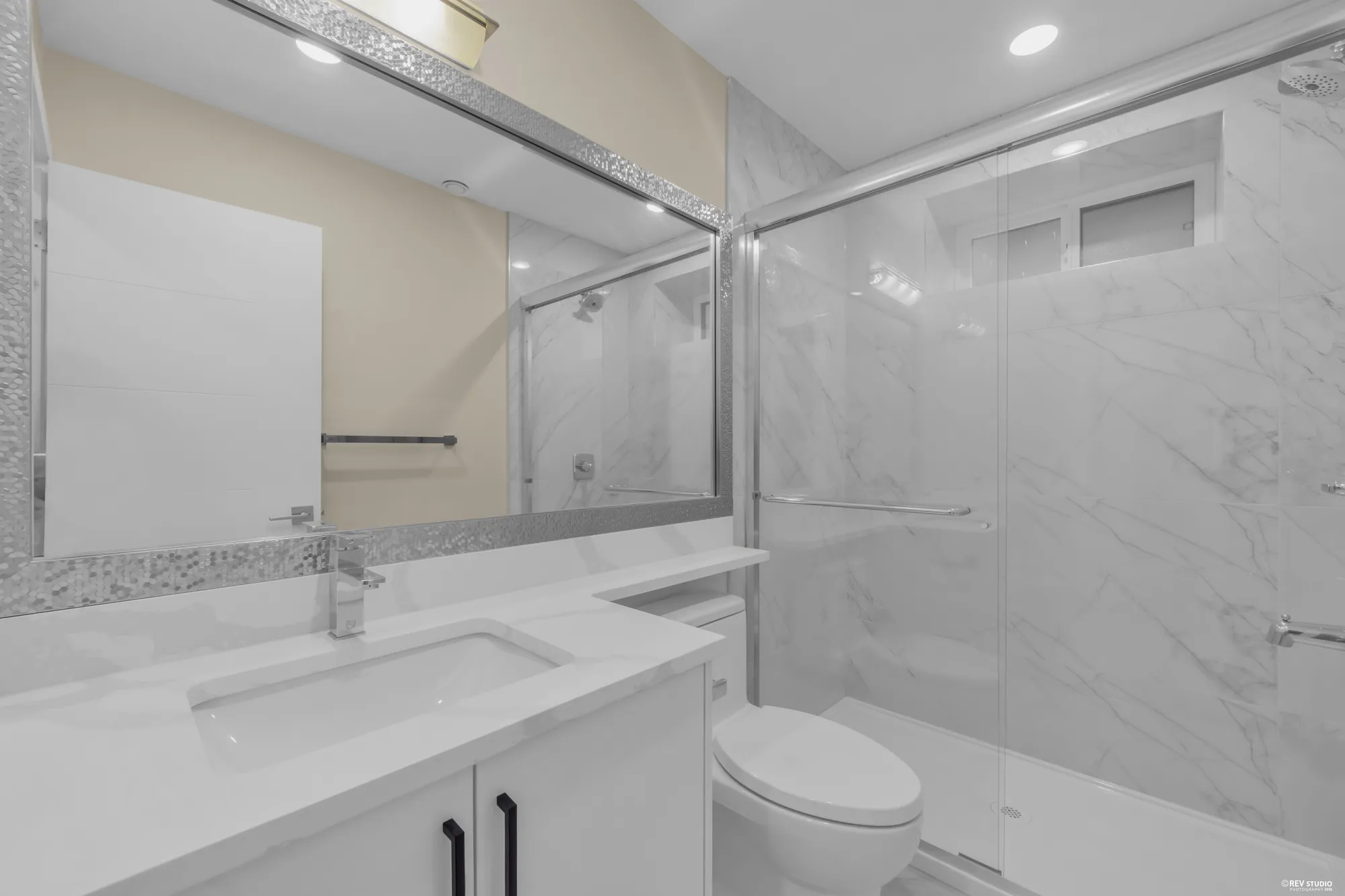 A lower bathroom with a tub and shower behind glass, a white vanity