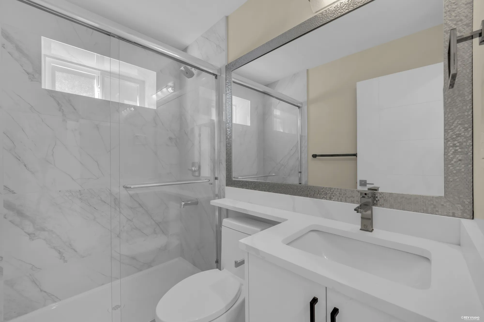A lower bathroom with a glass shower in marbled tile and a white vanity