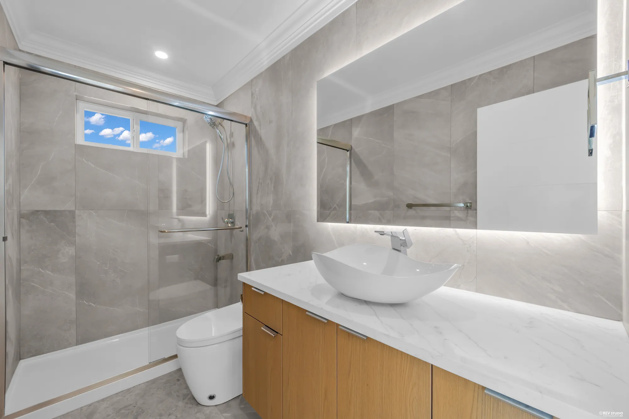 The main-floor bathroom: a vessel sink on an oak vanity, a lit mirror, a glass shower in grey tile