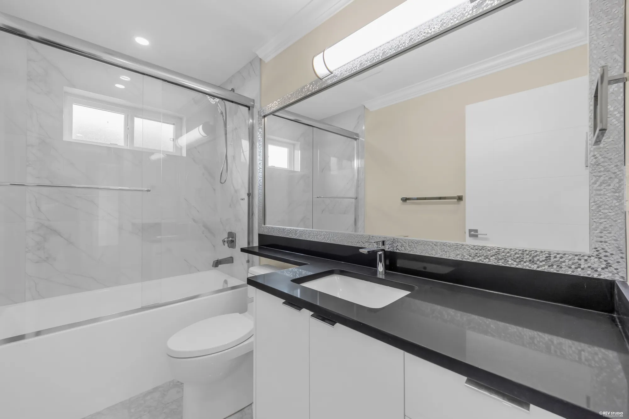 The hall bathroom: a tub and shower, a dark stone counter, a lit mirror