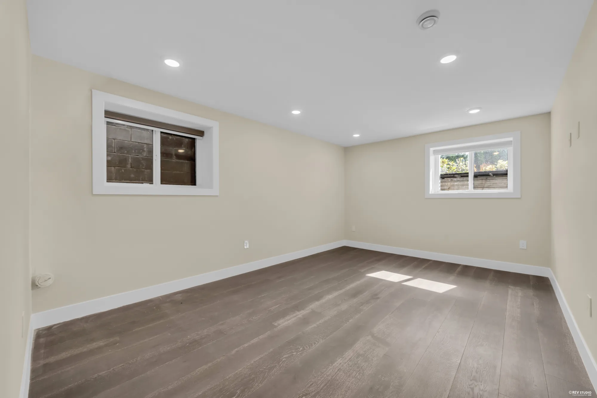 A lower bedroom with windows on two walls and a wood floor