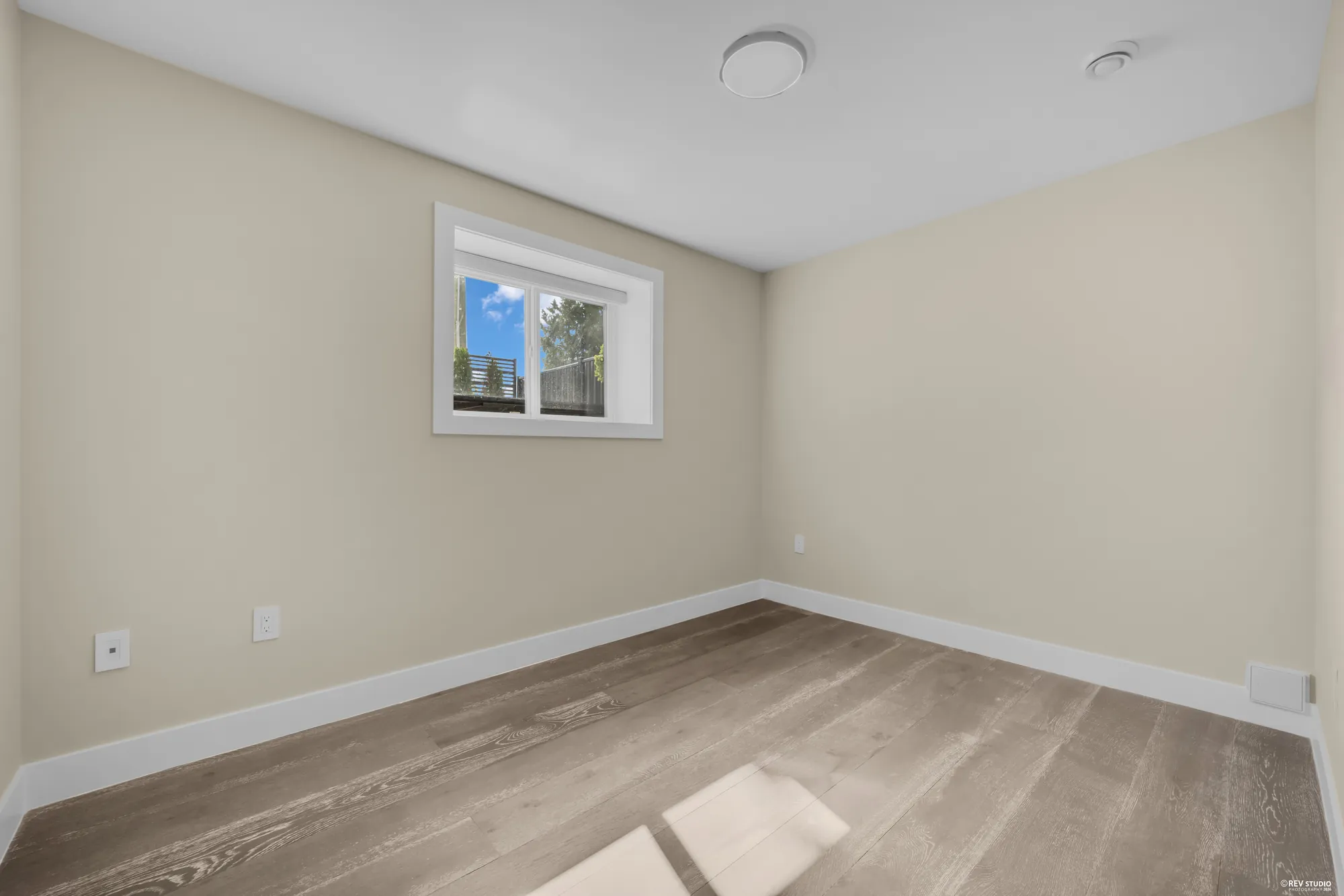 A lower bedroom with one window and a wood floor