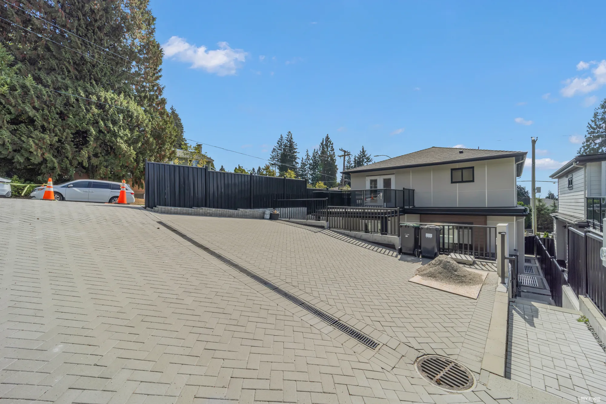 The paved court at the lane behind the house, the black fence along it, the neighbours beyond