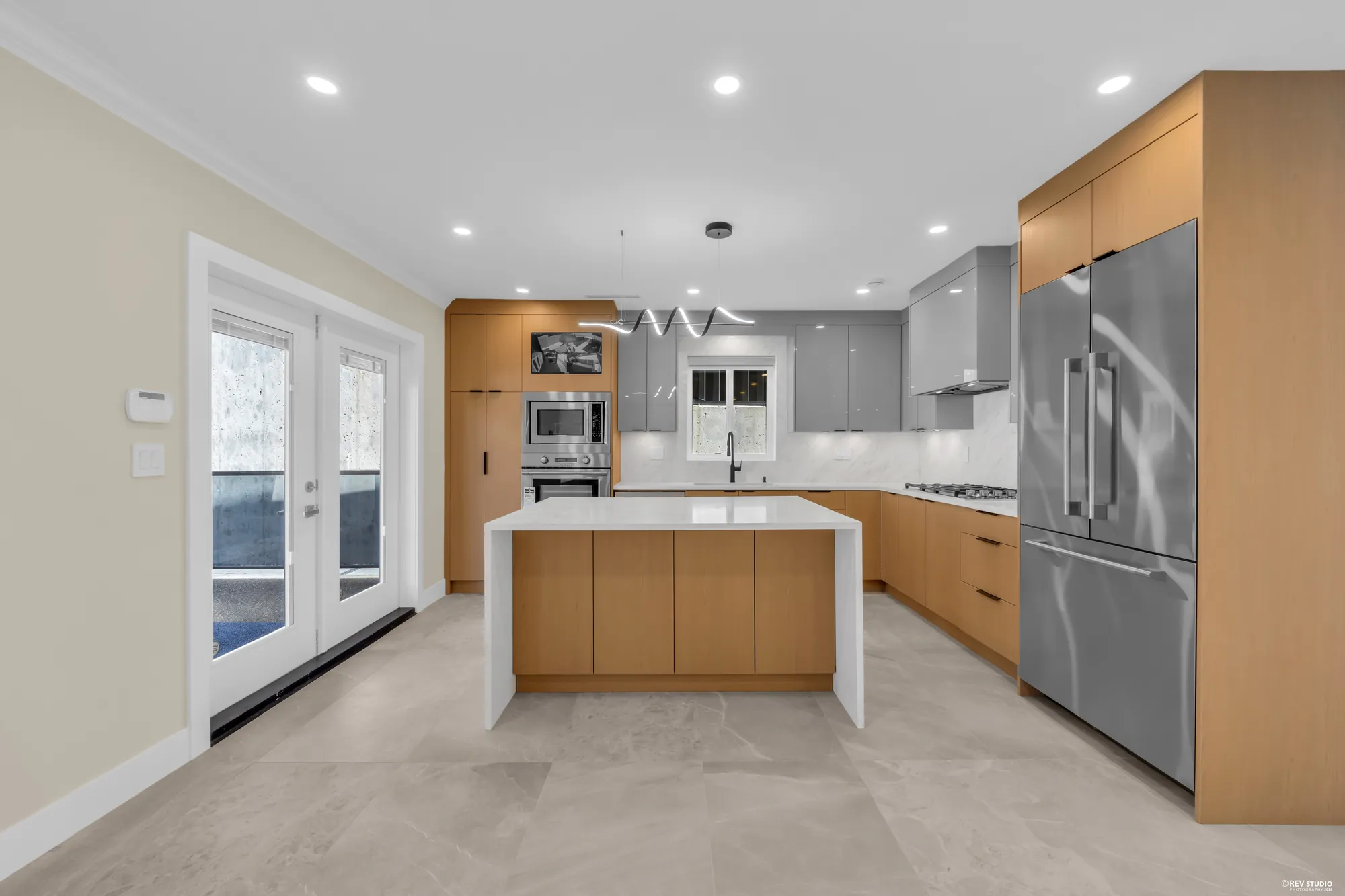 The kitchen: an oak island under white stone, grey upper cabinets, a stainless fridge and range, glass doors to the deck