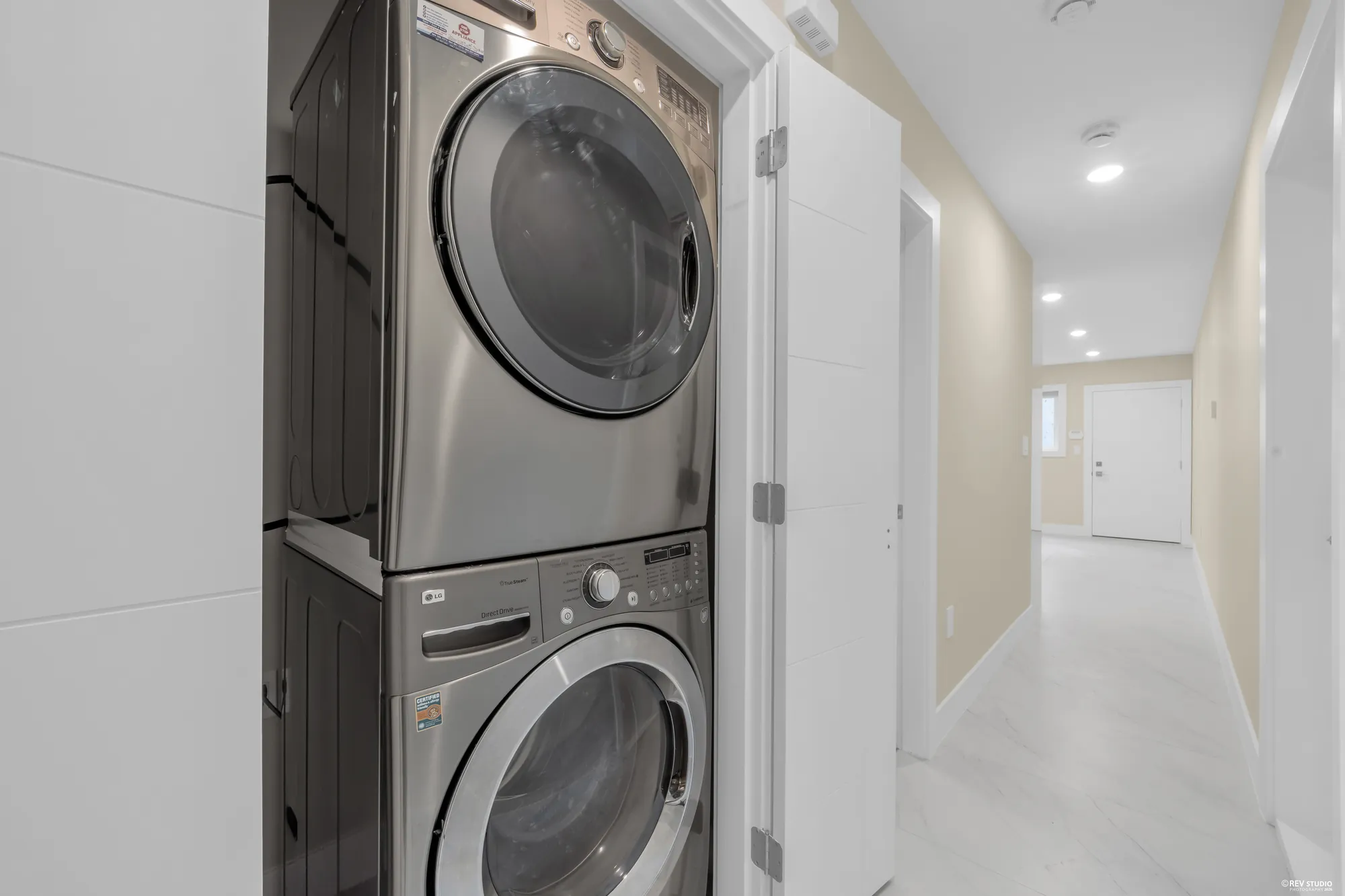 A stacked washer and dryer in a closet off the tiled lower hall