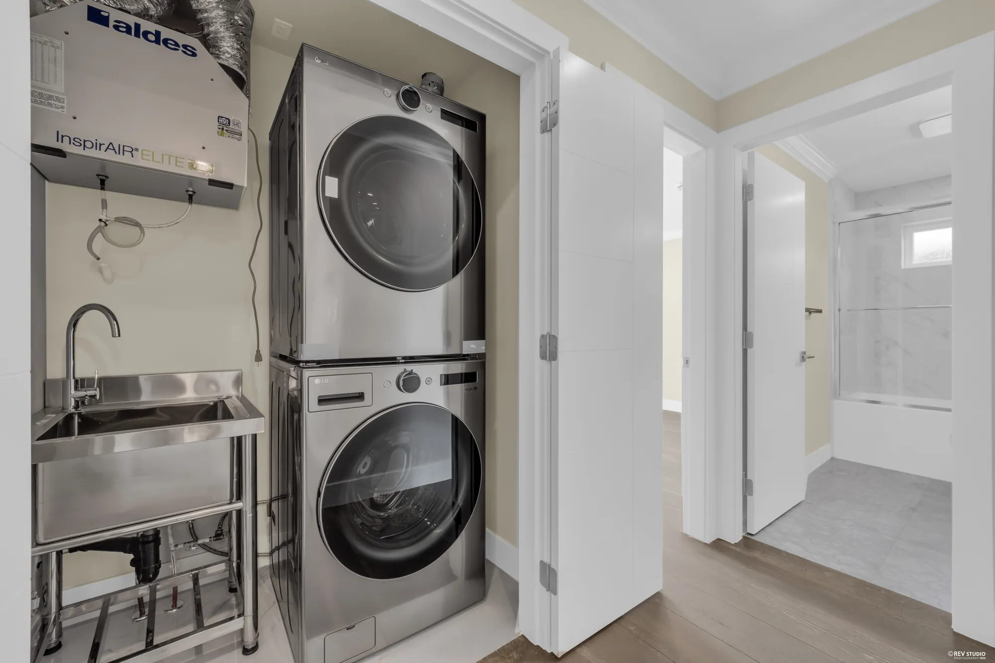A stacked washer and dryer in the upper hall with a utility sink beside them, a bathroom through the door