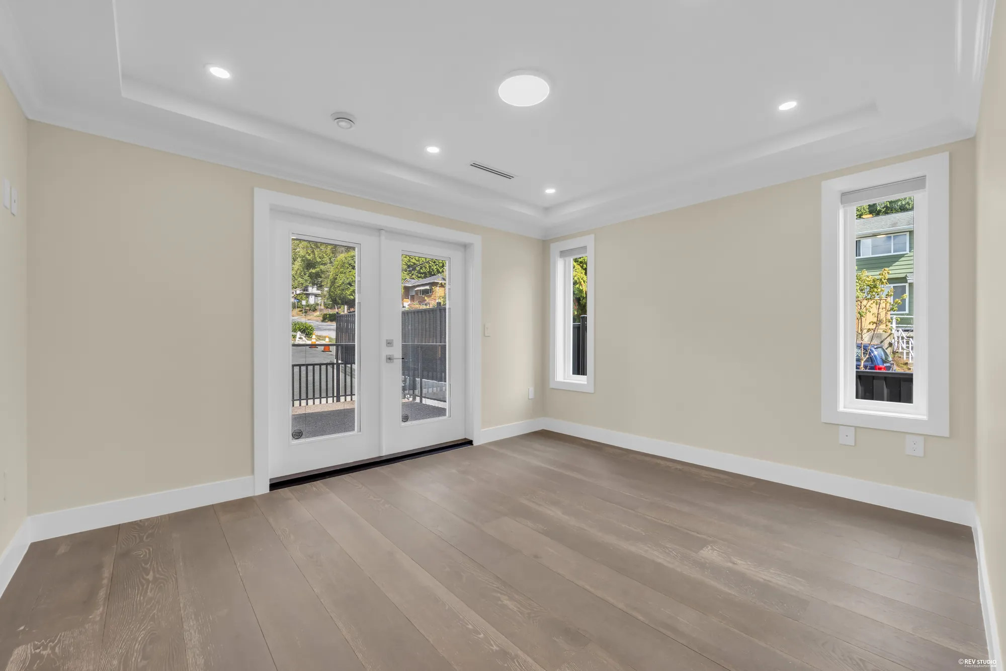 The primary bedroom: french doors to the balcony, windows either side, a tray ceiling