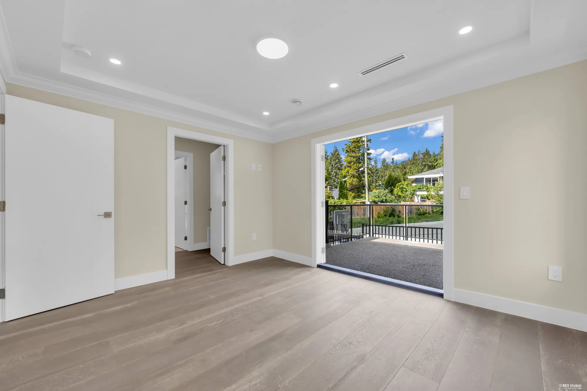 The primary bedroom with the balcony doors open, the lane and the trees beyond the rail