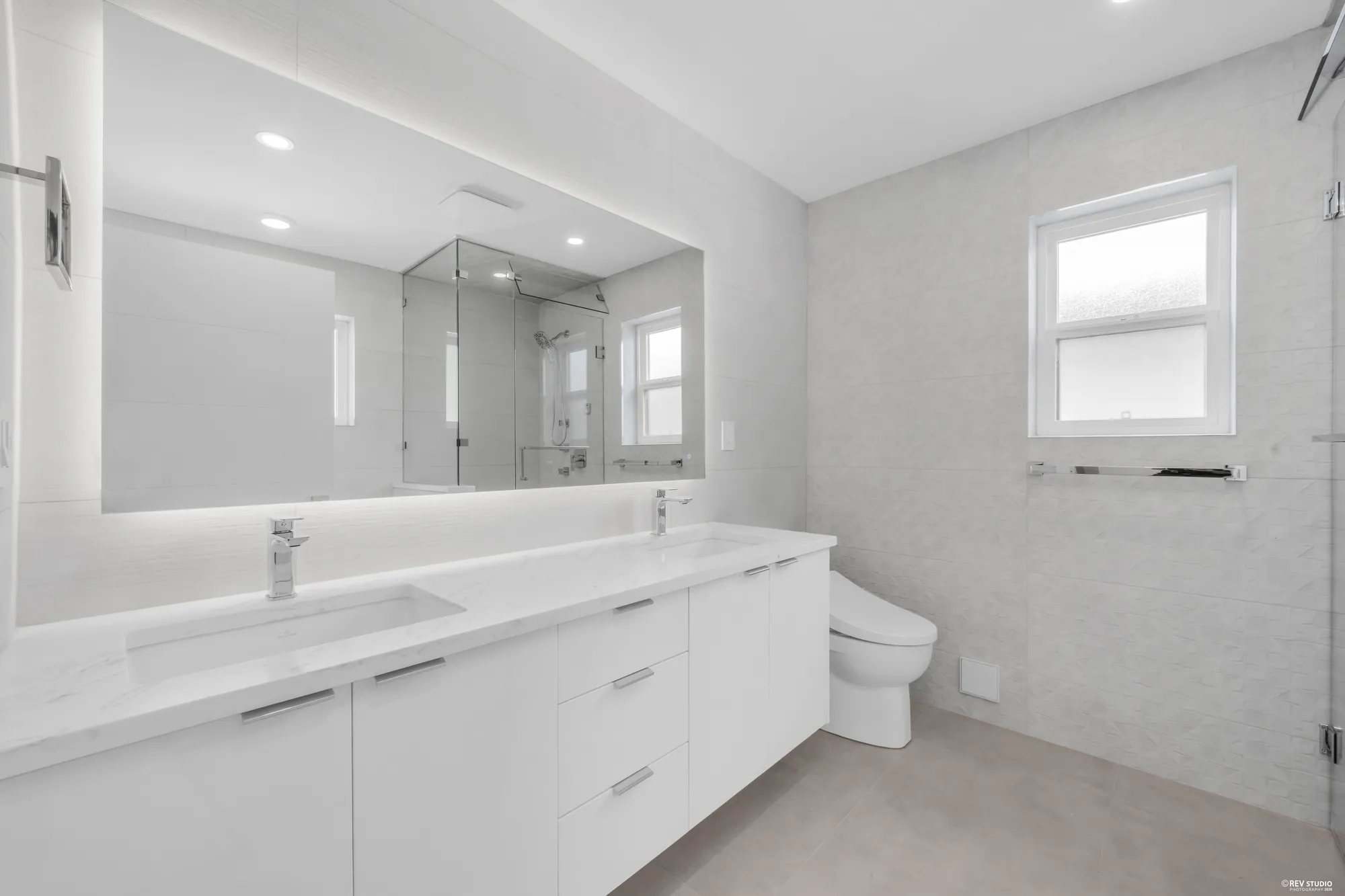 The primary bathroom: a long white vanity, a lit mirror, a glass shower at the end