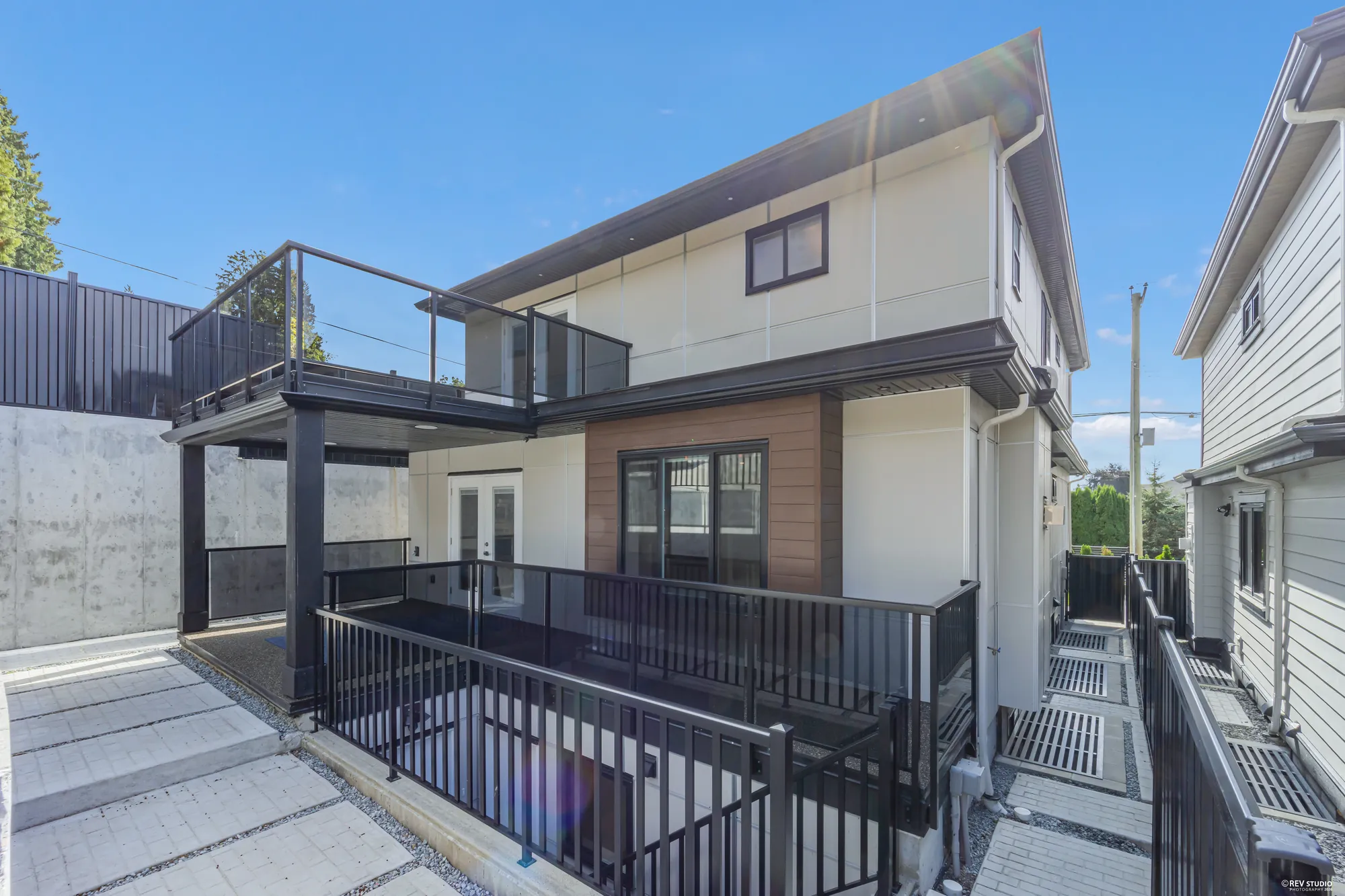 The back of the house: a deck with black railings off the main floor, a glass-railed balcony above, the covered patio beneath