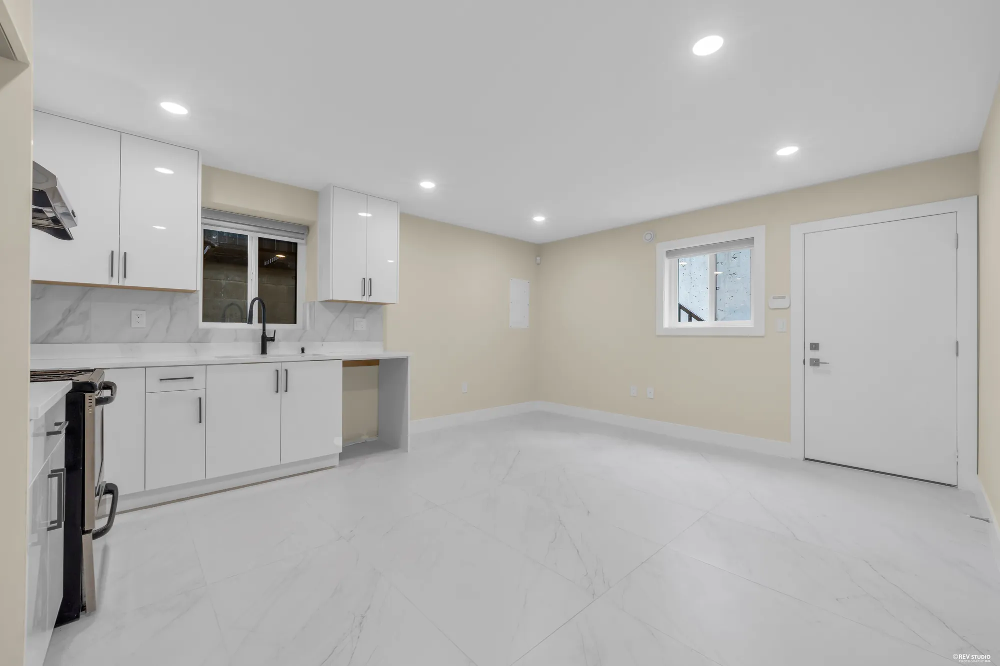 The lower kitchen: white cabinets, a window over the sink, a stainless range, a door on the right